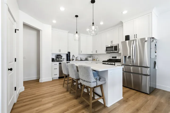 Modern kitchen featuring white cabinetry, stainless steel appliances, an island with seating, pendant lighting, and wood-finish flooring