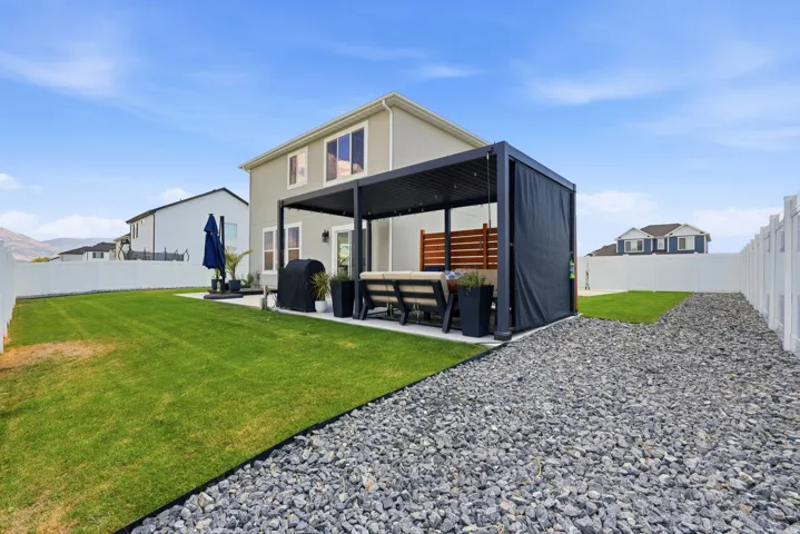 Expansive backyard featuring a lush lawn, white vinyl fencing, a concrete patio, a modern pergola with retractable shades, and a decorative gravel pathway