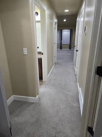 Hallway with carpet flooring, recessed lighting, and a bathroom entry featuring a vanity with a stone countertop