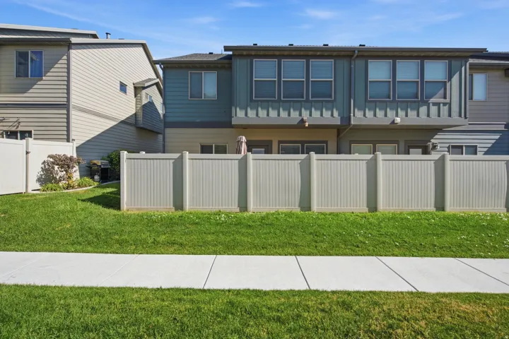 Townhome exterior featuring blue-gray and beige siding, white vinyl fencing, and a manicured lawn