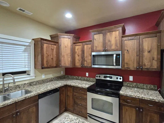 Kitchen featuring wood cabinetry, stainless steel appliances, speckled countertops, and a double basin sink