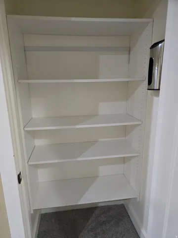 Built-in shelving unit with multiple white shelves and an integrated closet rod