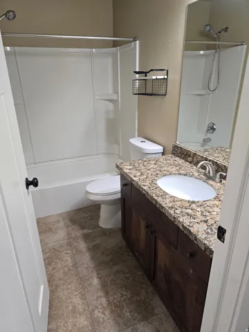 Granite-style countertop, integrated sink, wood-finish vanity, and tiled flooring