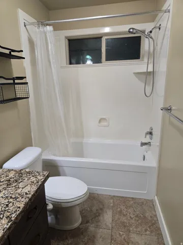 Tub and shower combination with a handheld showerhead, window, vanity with a stone finish countertop, and tile flooring