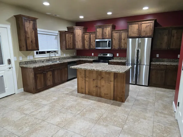 Kitchen featuring wood cabinetry, granite countertops, stainless steel appliances, a center island, and tiled flooring