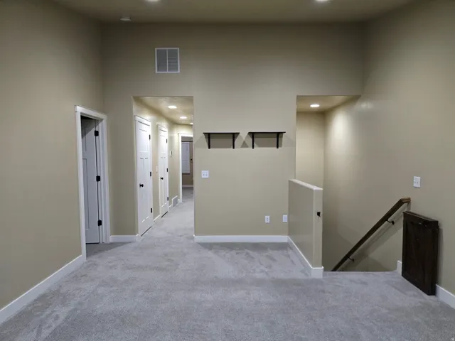 Plush gray carpeting with white baseboards, recessed lighting, and a wood-finish handrail