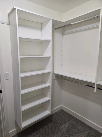 Built-in white shelving, integrated hanging rods, and dark gray carpet flooring