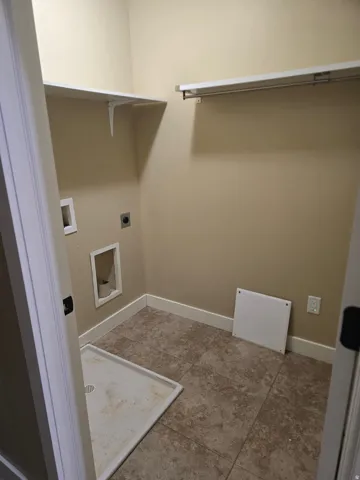 Laundry area featuring tile flooring, wall-mounted shelving, and a hanging rod