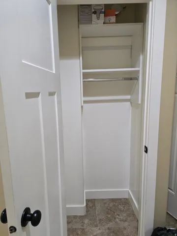 Recessed closet with built-in shelving, hanging rod, and tiled flooring