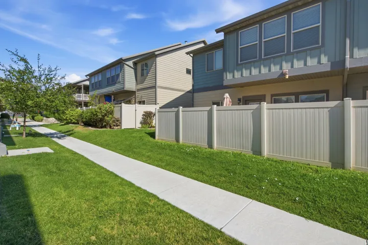 Landscaped green space featuring a concrete pathway and white privacy fencing