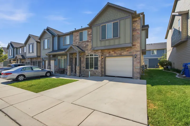 Multi-level townhome featuring a stone and siding exterior, an attached garage, a paved driveway, a covered entry, and a manicured lawn