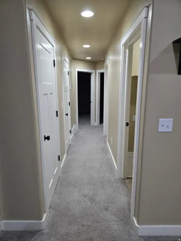 Hallway featuring recessed lighting, paneled doors with black hardware, and carpet flooring