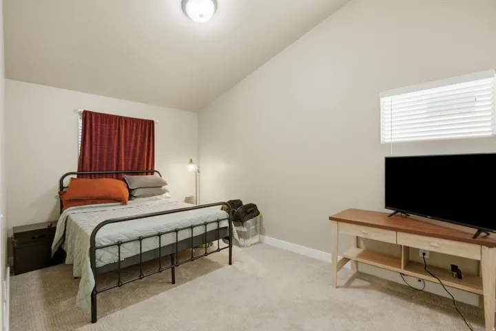 Carpeted bedroom featuring vaulted ceilings, neutral wall paint, and a window with horizontal blinds
