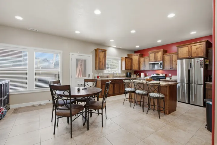 Spacious kitchen and dining area featuring recessed lighting, a kitchen island with seating, wood cabinetry, stainless steel appliances, and tile flooring