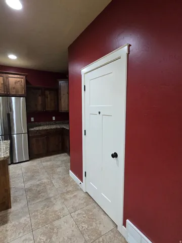 Stainless steel refrigerator, integrated wood cabinetry, granite countertops, tile flooring, and a flat-panel door with black hardware