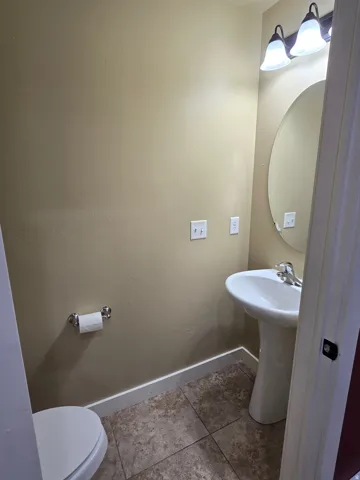 Pedestal sink with chrome faucet, oval mirror, wall-mounted light fixture, and tile flooring