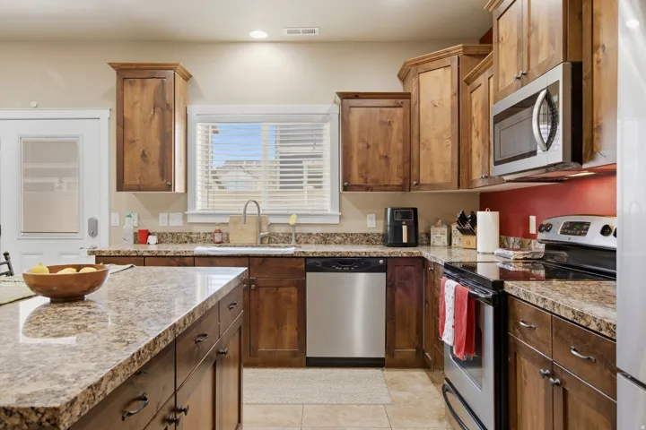 Kitchen featuring wood cabinetry, granite-finish countertops, stainless steel appliances, and tile flooring
