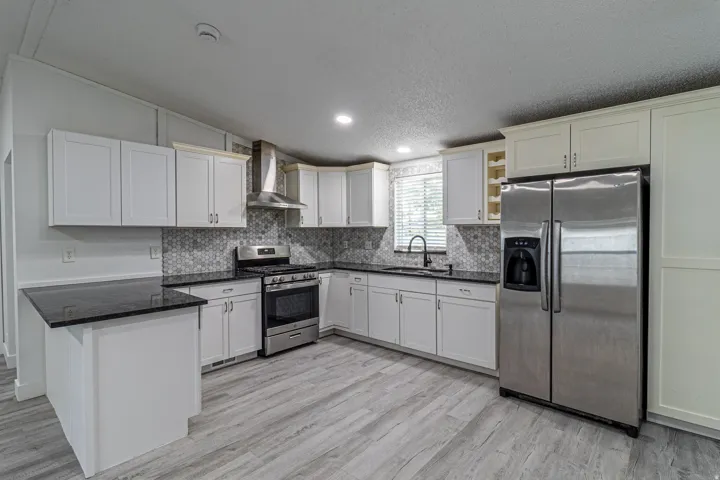 Kitchen featuring white cabinetry, black countertops, stainless steel appliances, a tile backsplash, and wood-finish flooring