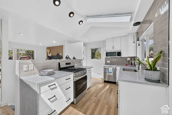 Modern kitchen featuring stainless steel appliances, light wood-finish flooring, white cabinetry, gray subway tile backsplash, and recessed lighting