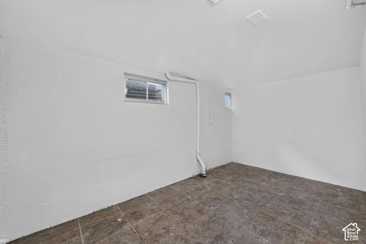 Spacious basement room featuring white-painted walls, a window providing natural light, and durable tile flooring