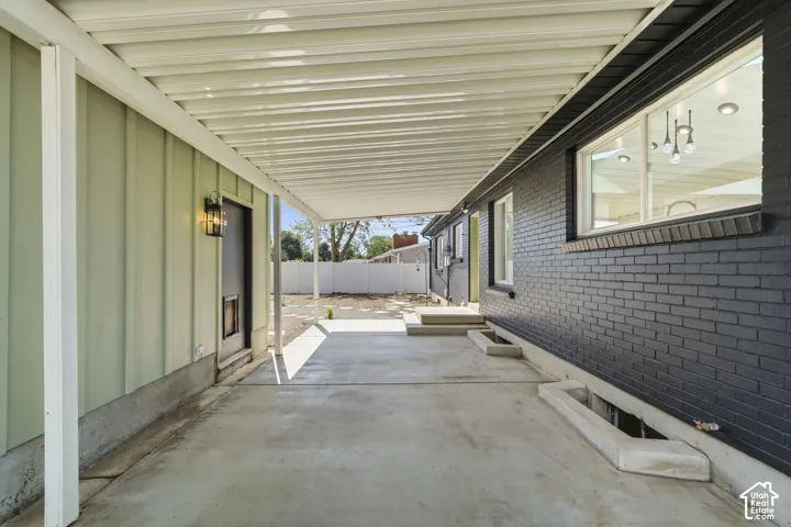 Covered patio area featuring a concrete surface, board and batten siding, dark brick exterior, exterior lighting fixture, and multiple windows