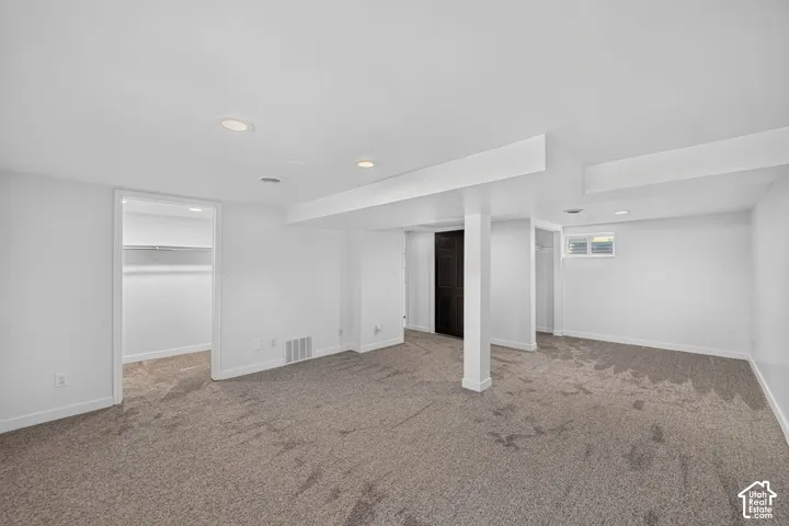 Spacious lower-level area with neutral carpeting, recessed ceiling lighting, a built-in closet with shelving, and a small window