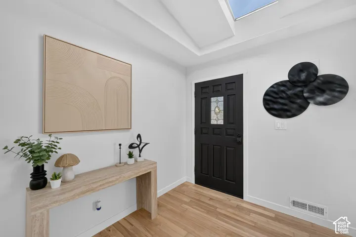 Entryway featuring a dark paneled door with a leaded glass insert, wood-finish flooring, a skylight, and white baseboards