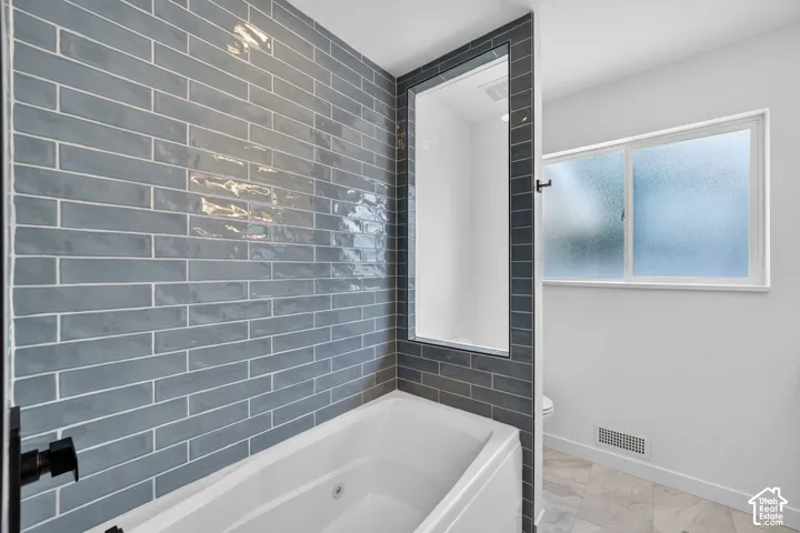 Bathroom featuring a built-in bathtub with matte black fixtures, full-height subway tile surround, and a frosted window