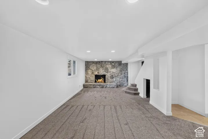 Spacious entertainment area featuring a stone-clad fireplace with hearth, recessed lighting, neutral carpeting, and a visible window