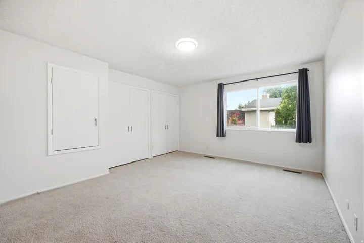 Bright interior featuring a large window, neutral carpeting, white walls, two sets of bi-fold closet doors, and a new ceiling-mounted light fixture