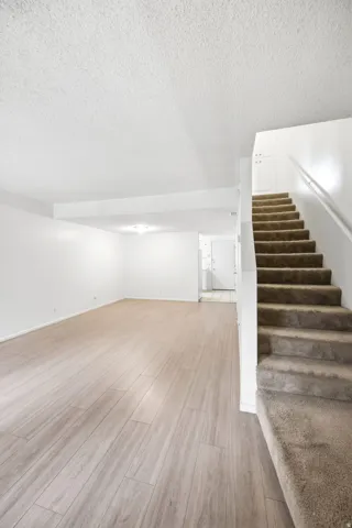 Spacious room with wood-finish flooring, white walls, and a newer bright light fixture