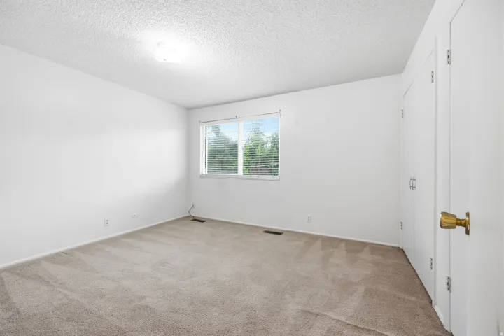 Bright room featuring light beige carpet, white walls, and a window with horizontal blinds