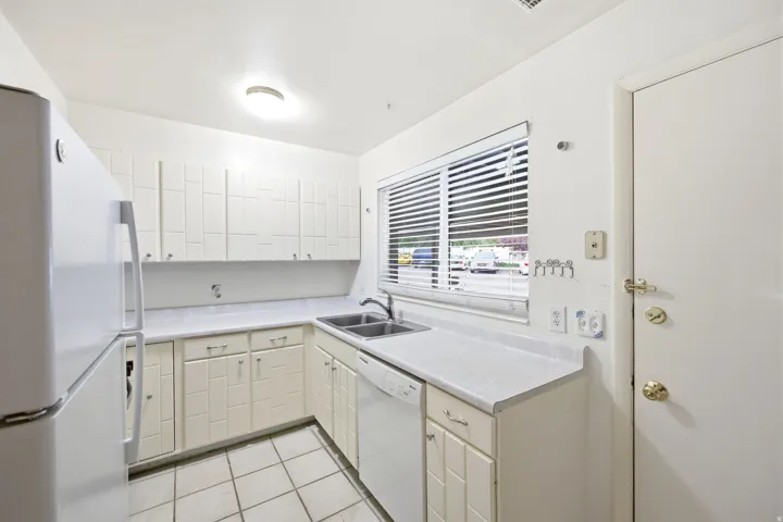 Kitchen featuring white tile flooring, white cabinetry, a double basin sink, white countertops, and a white dishwasher