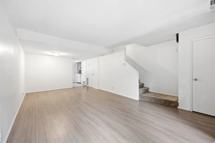 Spacious living area featuring wood-finish flooring, neutral white walls, and a ceiling light fixture