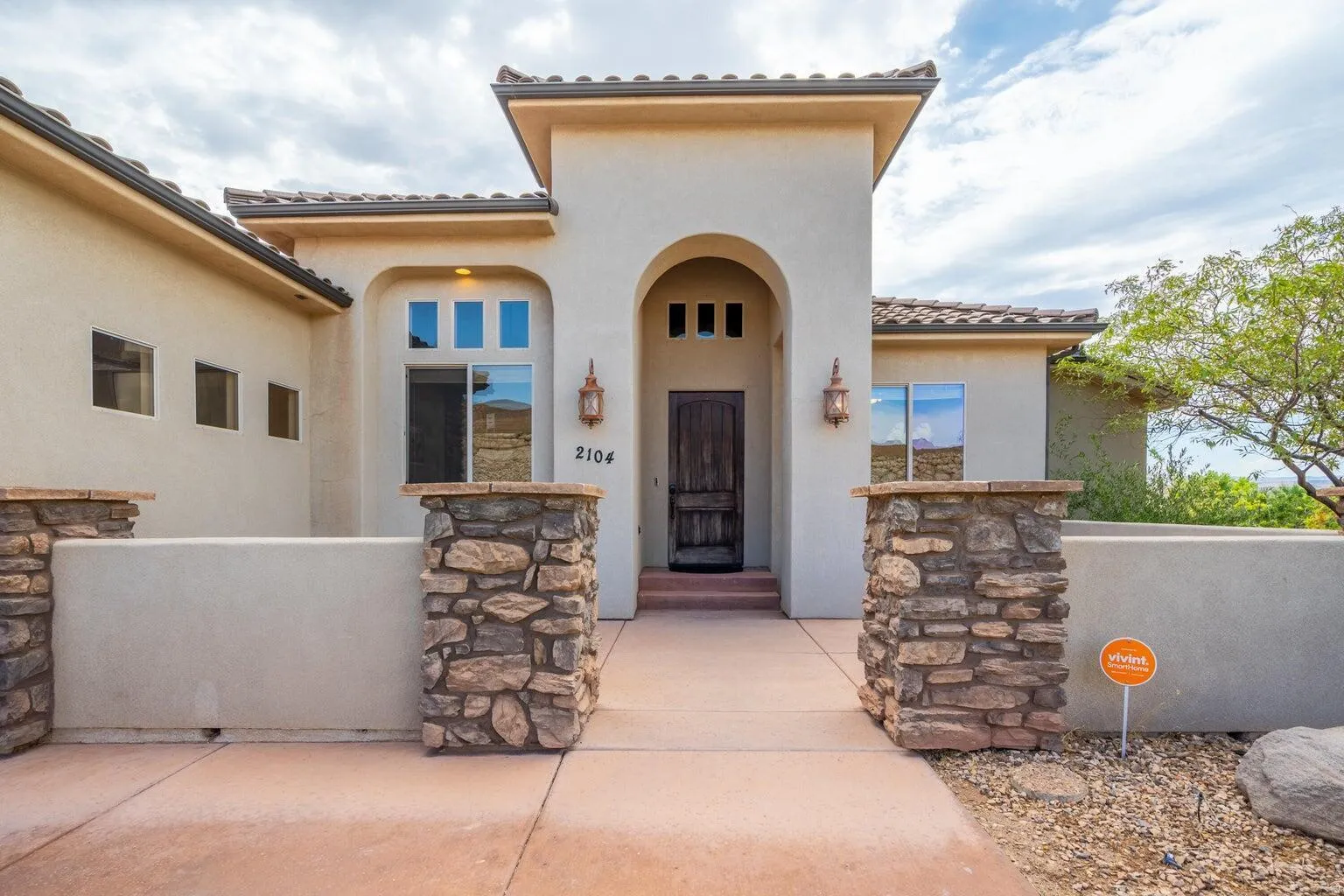 Stucco exterior featuring an arched entryway with a dark wood-finish door, stone-clad pillars, and a Spanish tile roof