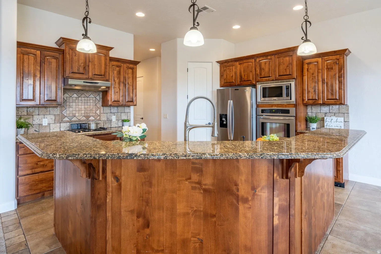 Kitchen featuring a curved central island with granite countertops, wood cabinetry, and stainless steel appliances, including a built-in oven and microwave