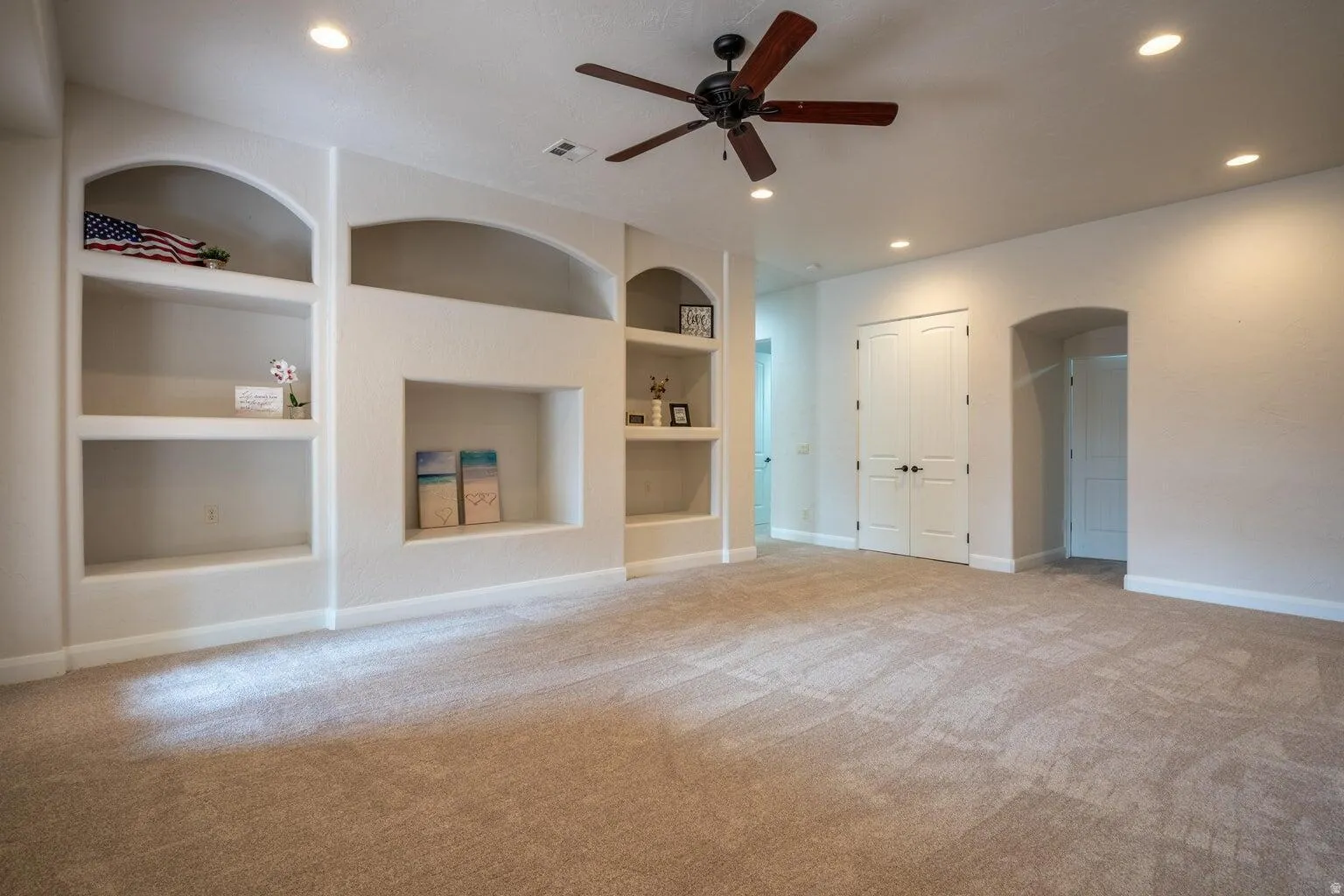 Spacious room featuring neutral carpet flooring, recessed lighting, and a dark-toned ceiling fan