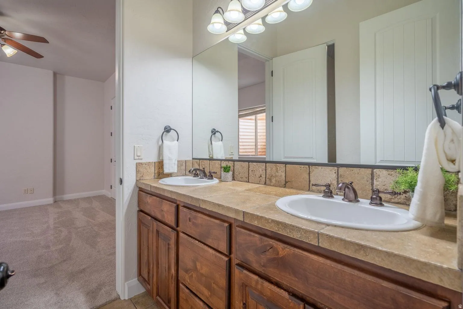 Double vanity with integrated sinks, a tiled countertop and backsplash, and individual bronze-finish faucets