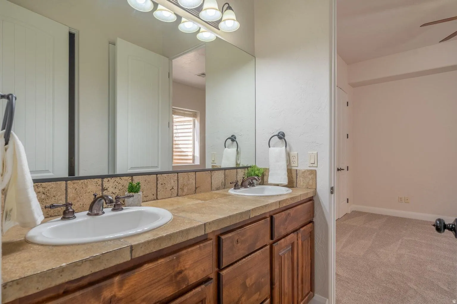 Dual vanity with integrated sinks, wood cabinetry, stone-finish countertop, and tiled backsplash