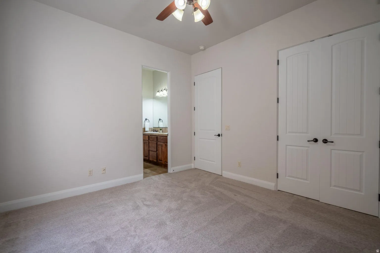 Carpeted interior room with an attached bathroom featuring a dual vanity and wood-finish cabinetry