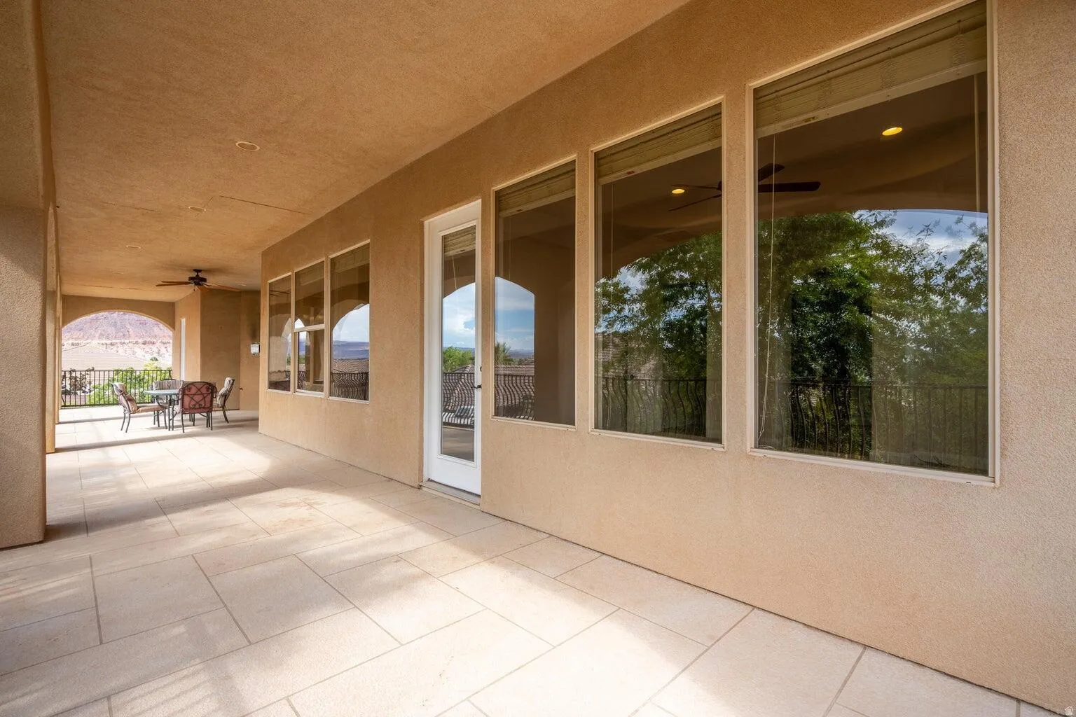 Spacious covered patio with light-colored rectangular tile flooring, stucco walls, and a recessed ceiling with a ceiling fan