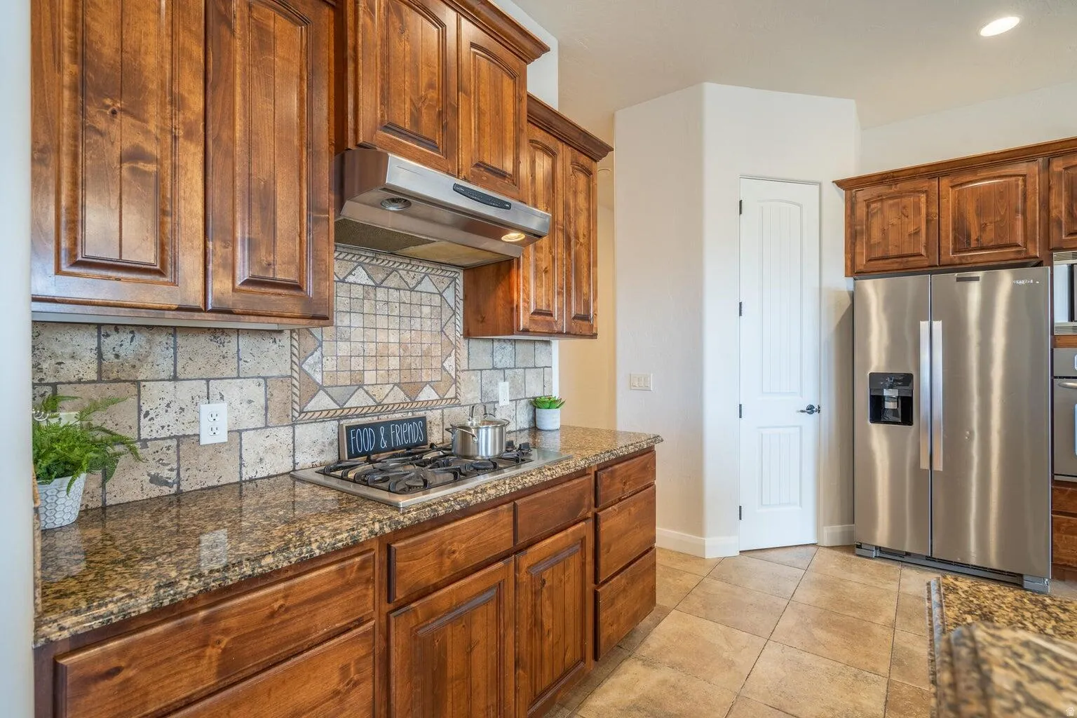 Kitchen featuring wood cabinetry, a built-in gas range, stainless steel range hood, granite countertops, and a tiled backsplash with decorative inset