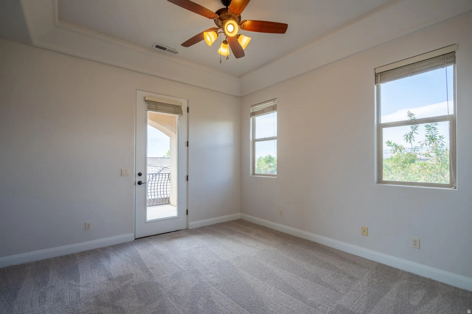 Tray ceiling with recessed lighting above a spacious room featuring light-colored carpeting, multiple windows, a glass-paneled door, and a ceiling fan with integrated lighting