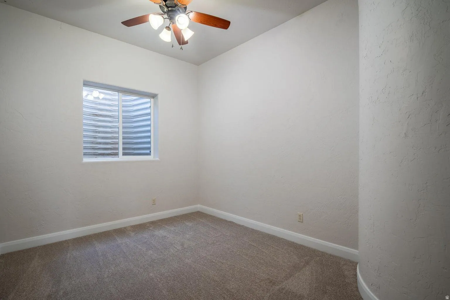 Carpeted interior space featuring a single window, white baseboards, and a ceiling fan with integrated lighting