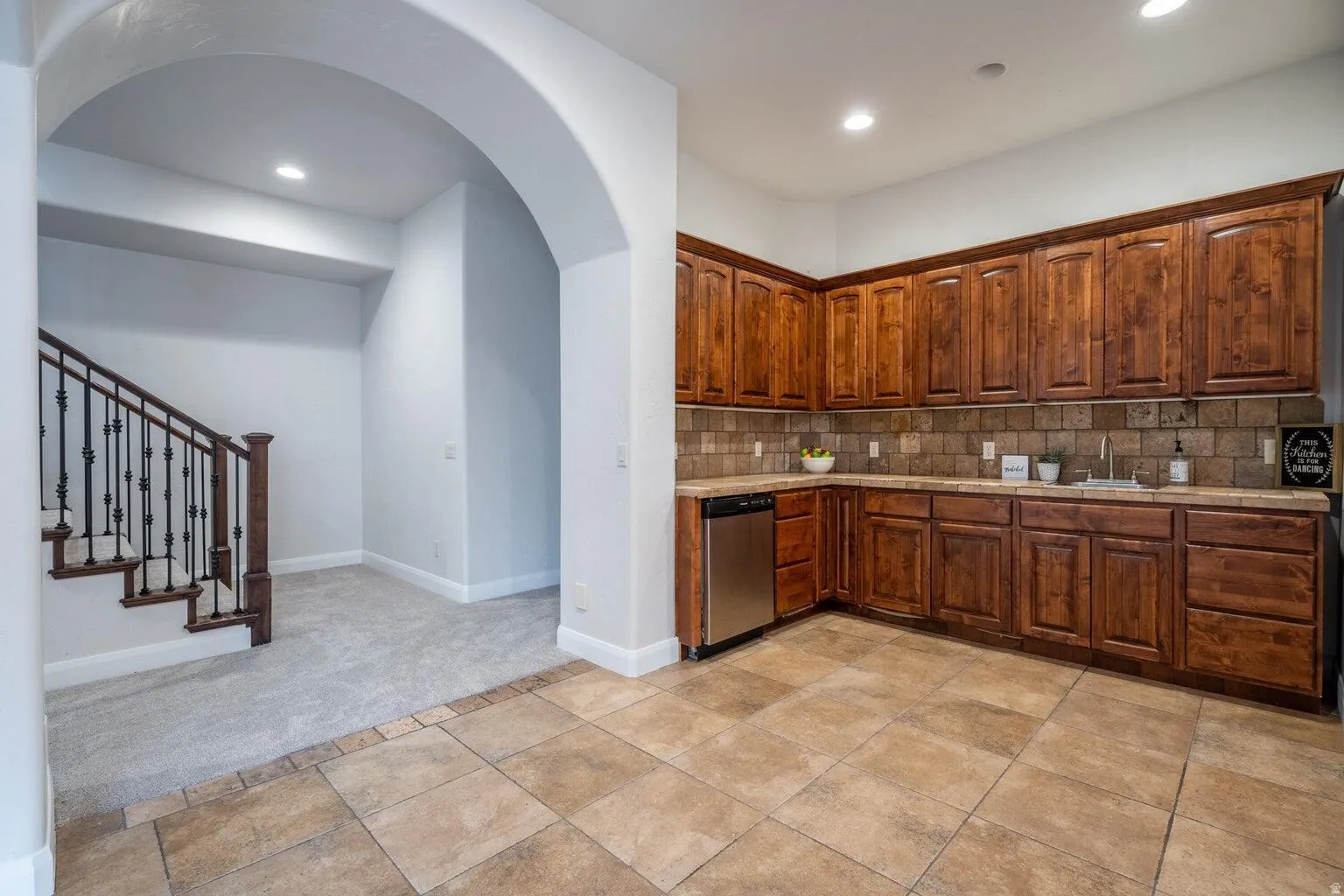 Kitchenette featuring wood cabinetry, stone-finish countertops, tile backsplash, stainless steel dishwasher, and a stainless steel sink