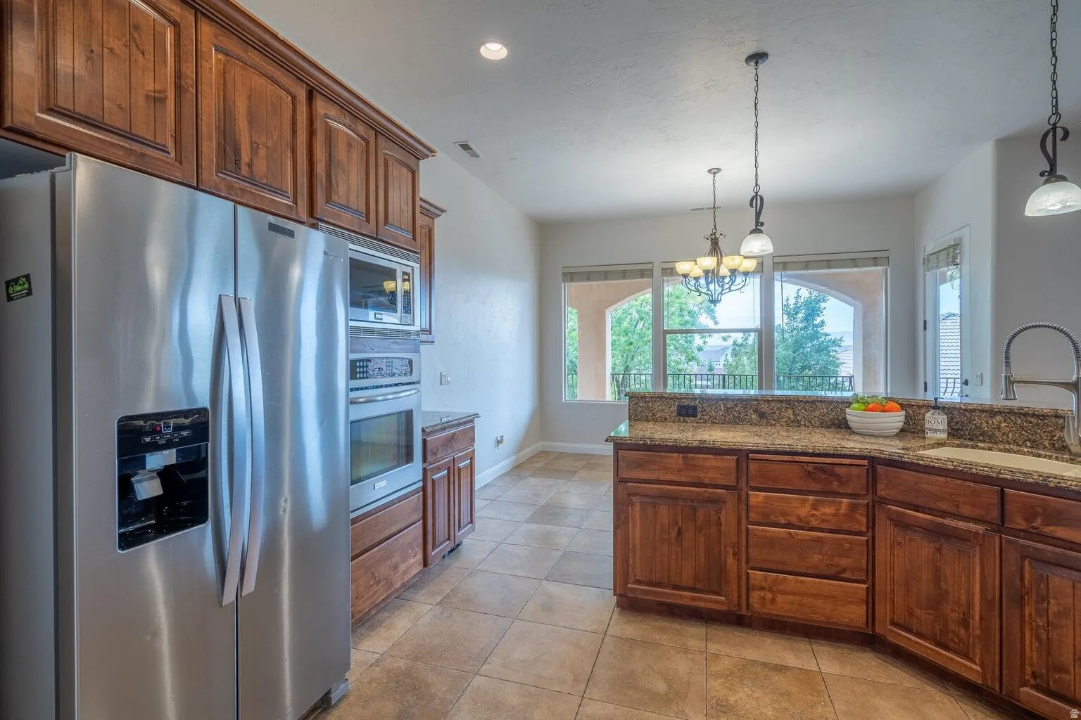 Kitchen featuring stainless steel appliances, wood cabinetry, granite countertops, and tiled flooring