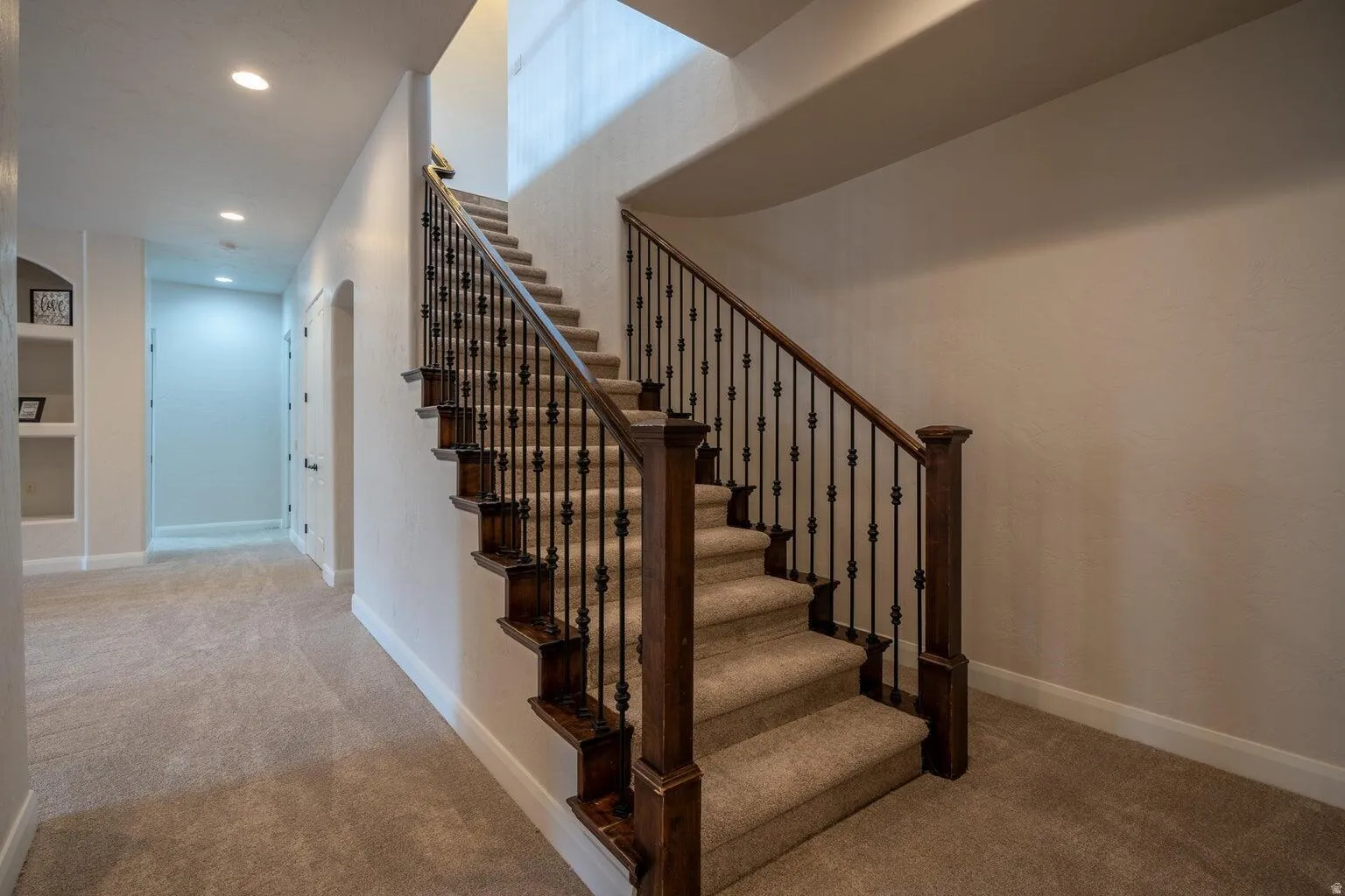 Staircase featuring dark wood handrails and newel posts with wrought iron balusters