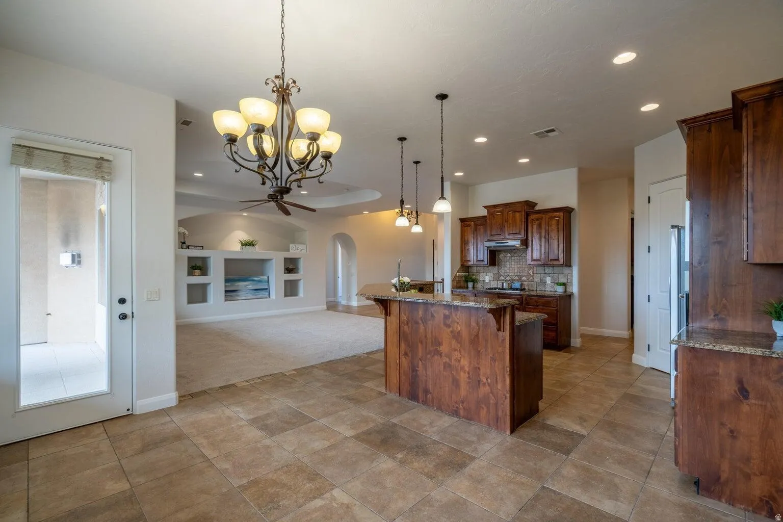 Open-concept floor plan featuring a kitchen with warm wood cabinetry, granite countertops, and tile backsplash