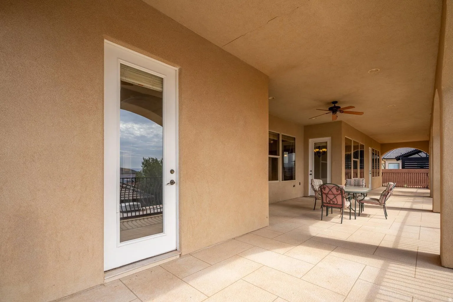 Expansive covered patio featuring light-toned tile flooring, stucco walls, and a ceiling fan