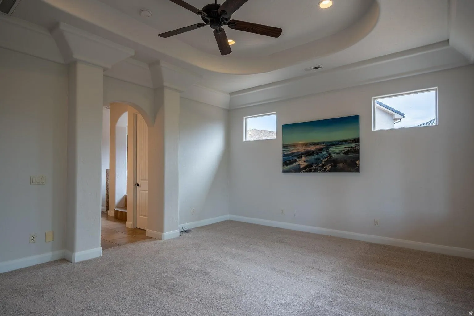 Spacious room featuring a tray ceiling with recessed lighting and a ceiling fan, carpet flooring, transom windows, and an arched entry